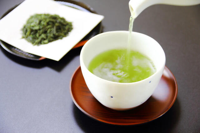 茶葉と緑茶を入れる様子を表す写真。緑茶は玉露・煎茶・番茶・抹茶・ほうじ茶などの種類があります。ビタミンCの含有量が多いのが特徴です。抗酸化作用・体脂肪低下・リラックス作用などの効能効果が期待できます。