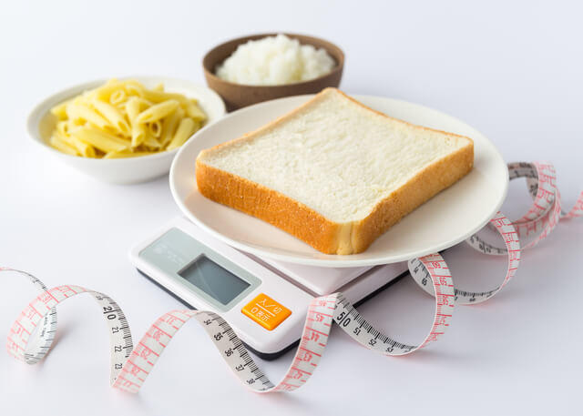 写真：摂取エネルギーを制限するために炭水化物の食パンの重さを計量器で測っている写真。糖質制限によりカロリーを減らすことをあらわしている