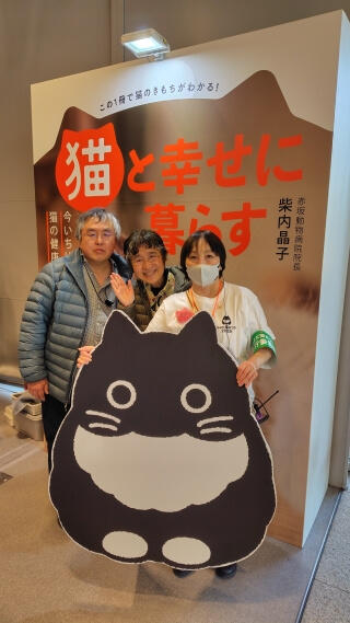 写真:著者が、友人の柴内晶子さんとともに、同氏の著書「猫と幸せに暮らす」のパネルを背景に撮影した写真