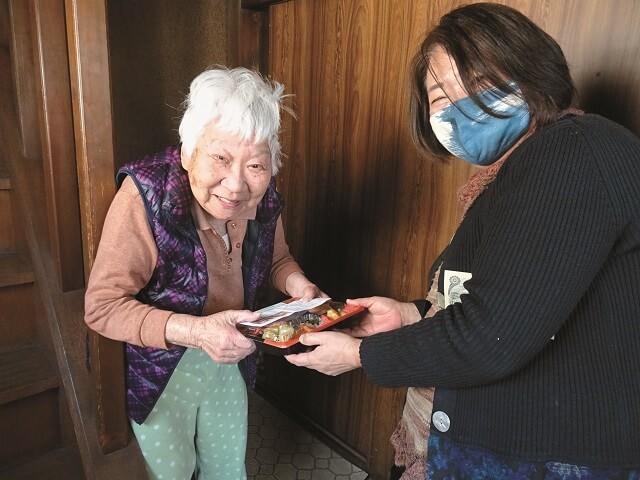 写真7:認知症の方の見守りも兼ねて弁当の宅配を行う様子を表わす写真。