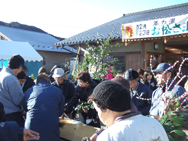 写真5:1年間の感謝の意を込めた村のイベントであるお松さま祭りの様子を表す写真。組合が協力し、門松やしめ飾りなど迎春用品の販売のほか、体を温める数種類の大鍋や特産品が販売される。
