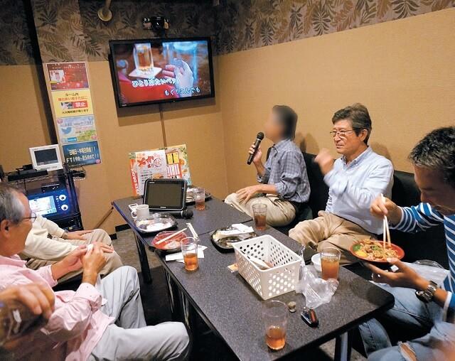 写真7:仕事後のランチの様子を表す写真。メンバーに人気のカラオケ昼食の様子。食事の後カラオケが始まる。