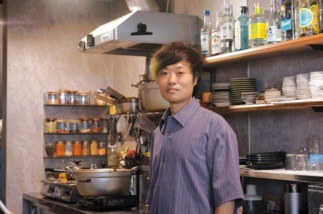 丸五スパイスアップのカウンターに立つはっぴー代表のしゅとうよしひろさんの写真。