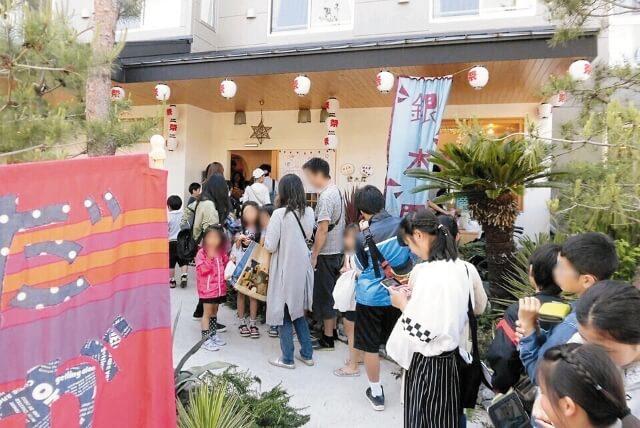 祭りの日、駄菓子屋の行列に並ぶ地域住民の写真。
