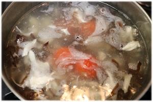 写真：鍋にきくらげ、湯剥きしたミニトマト、ガラスープ顆粒タイプ、しょう油を加え、塩こしょうで味を調える様子を表す写真。