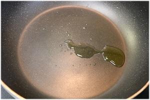 写真：フライパンでオイルサーディンの漬け油を熱する様子を表す写真。