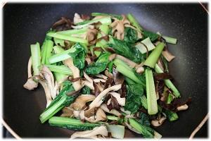 写真：フライパンでまいたけ、きくらげ、小松菜を炒める様子を表わす写真。
