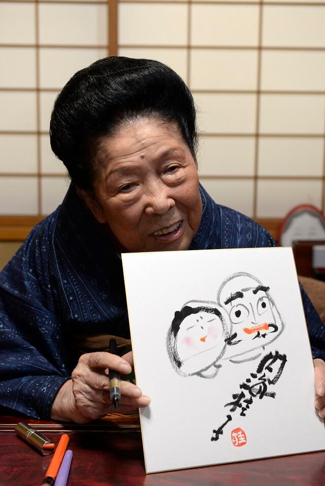 写真2：内海桂子氏のサイン色紙を表す写真。描かれた夫婦達磨の頬紅は口紅を使う。