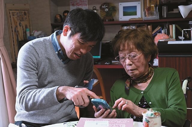 写真6：榮子さんが孫の康二郎さんからLINEを教わる様子を表す写真。
