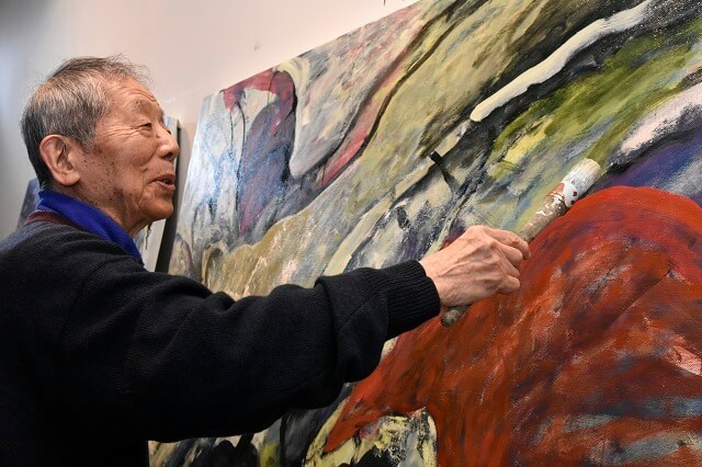 写真6：制作中の絵に白い絵の具で筆を入れる野見山さんの様子を表す写真。