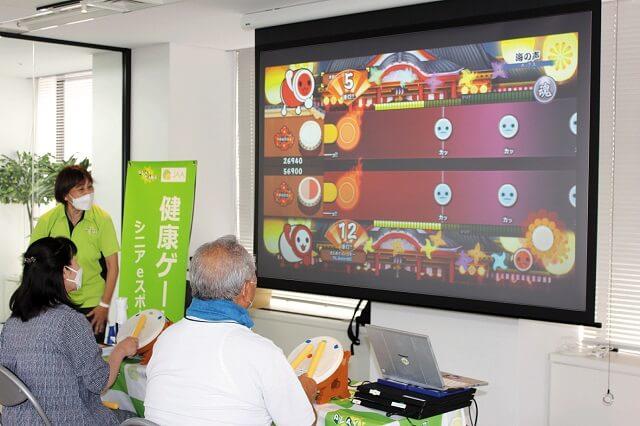 写真4、「健康ゲーム(eスポーツ)体験会」で『太鼓の達人®』を楽しむ参加者の様子を表す写真。取材協力:株式会社プレイケア。