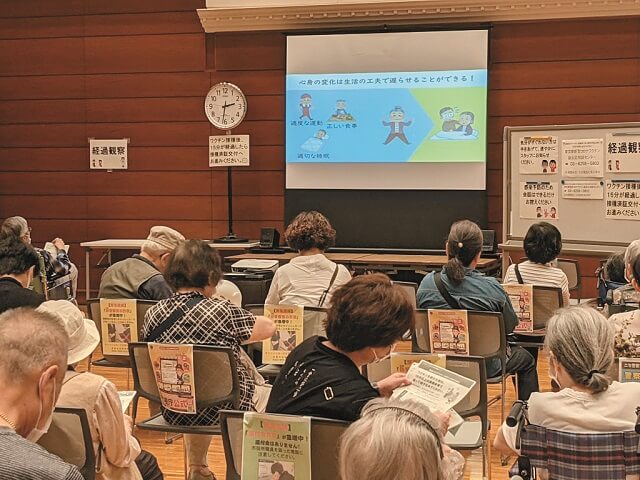 写真5：新型コロナ ウイルスワクチンの集団接種会場の待機スペースで教材の動画を上映し、健幸啓発を行う様子を表わす写真。