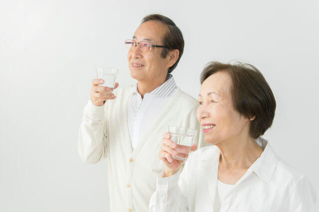 健康のために水を飲む高齢夫婦の様子を表す写真。