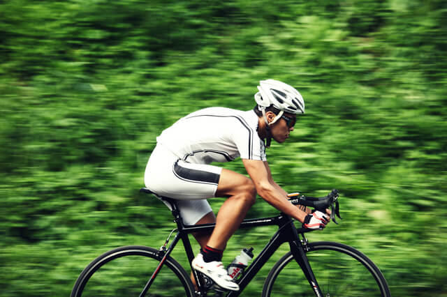競技用自転車で疾走する男性の写真。運動強度が上がっていくと血中乳酸濃度が顕著に上昇することを表現している。血中乳酸濃度が急増する領域を乳酸性閾値という。