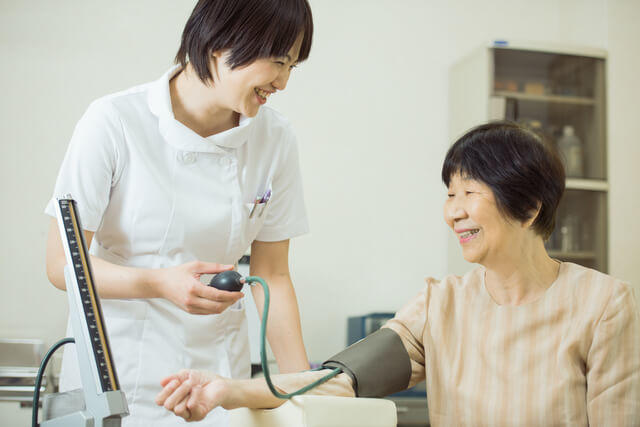 健康診断で動脈硬化の予防に重要な健康診断項目である血圧を測る女性の写真。人は血管とともに老いると言われています。動脈が固くなったり瘤ができる動脈硬化は、肥満、高血圧、脂質異常症(高脂血症)、糖尿病等の生活習慣病により促進されるので、予防・管理することが大切です。定期的な健康診断で健康状態を把握することが大切です。