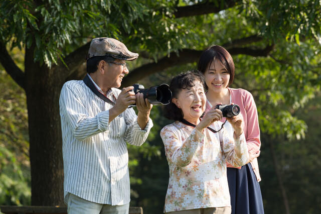 趣味のカメラを楽しむ高齢者夫婦と子の写真。高齢者の運動機能の向上を図ることは、趣味などの活動を通じて身体活動量を増やし、活動的な生活を送ることを促すこと表す。