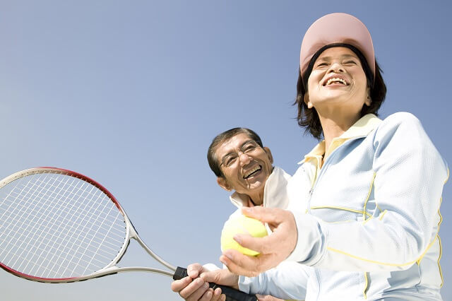 写真2：笑顔でテニスをする高齢男女