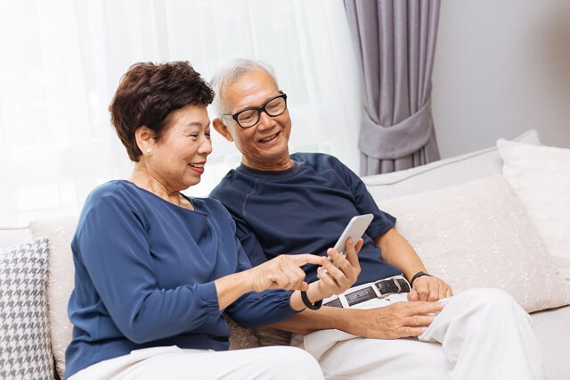 写真２：高齢夫婦が居間のソファでスマートフォンを一緒に見ている写真