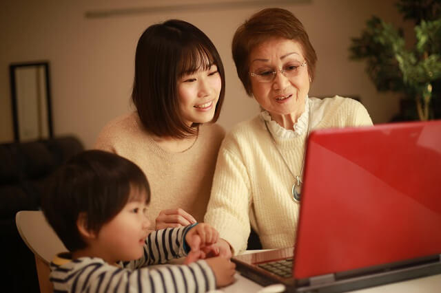 写真：子供と一緒にノートパソコンをつかっている高齢女性の写真