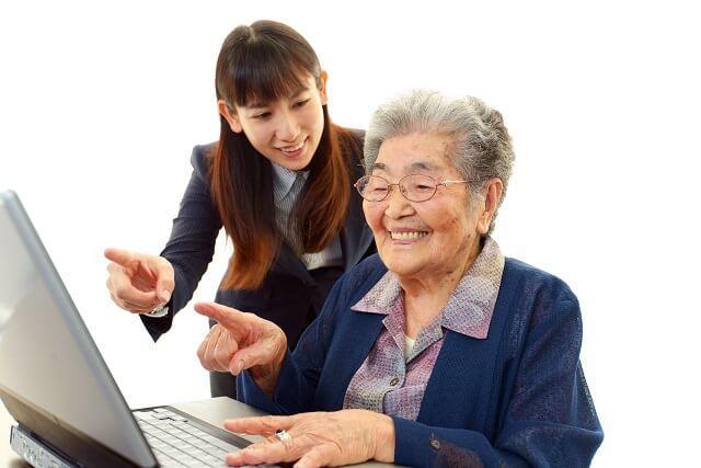 写真：高齢女性にパソコンの使い方を教えている若い女性の写真