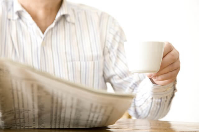 写真：コーヒーを片手に新聞の健康情報をみている男性の写真