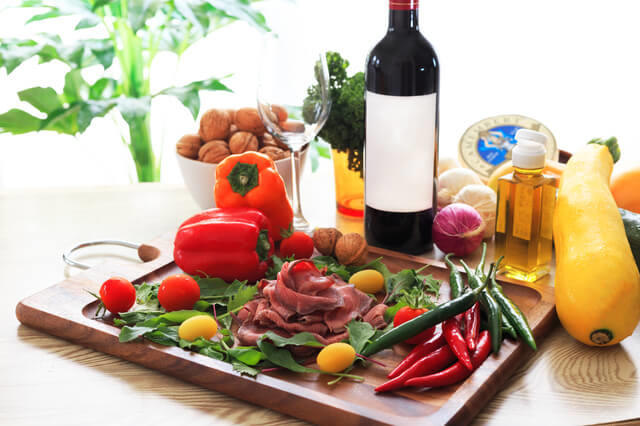 写真：地中海食の特徴を表す写真。地中海食は緑黄色野菜が豊富で、オリーブオイル、ナッツを良く使い、食事と一緒に赤ワインを飲むことを示す。