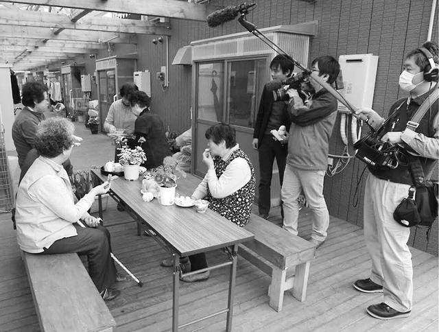 写真:釜石市の縁側デッキでの「お茶っこ」の様子をテレビの取材班が撮影している風景写真。