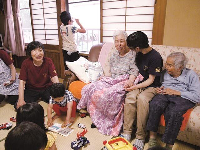 写真:年齢や障害の有無などにかかわらず、誰もが住み慣れた地域でデイサービスを受けられる場所「富山型デイサービス」での風景を表す写真。左端が開設者である惣万佳代子氏。