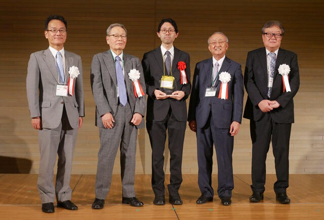 小林正樹氏の表彰式の様子を表す写真。